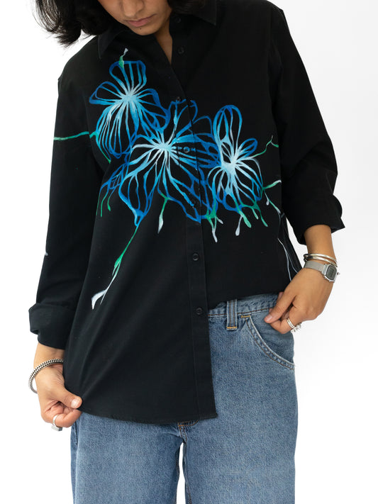 Person wearing a black shirt with blue floral designs and blue jeans on a white background