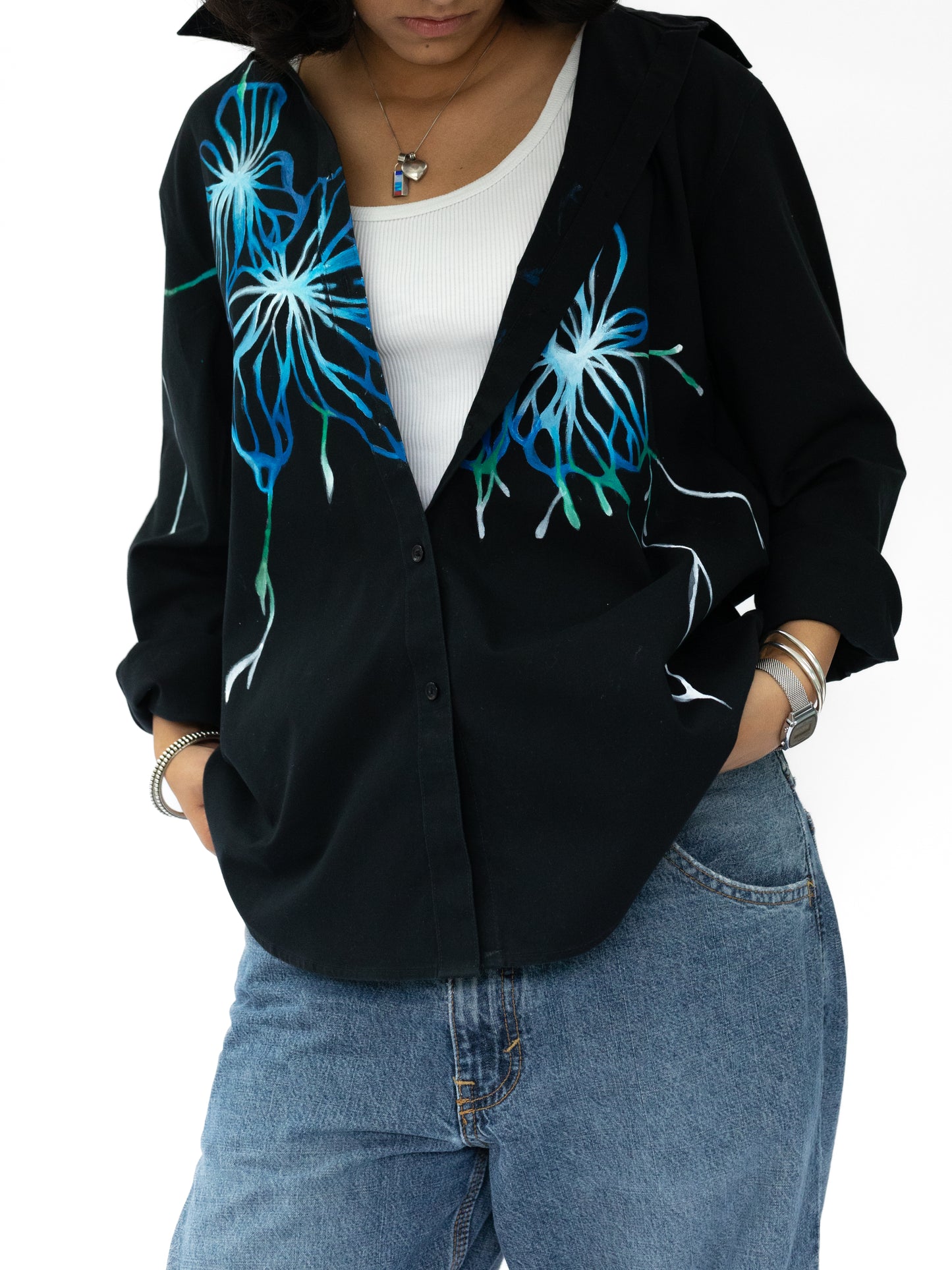 Person wearing a black cardigan with blue floral designs, white shirt, and blue jeans on a white background